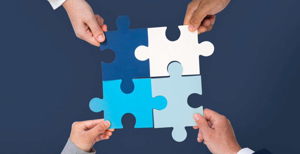 Ręce układające kolorowe puzzle w zespole, symbolizujące współpracę.